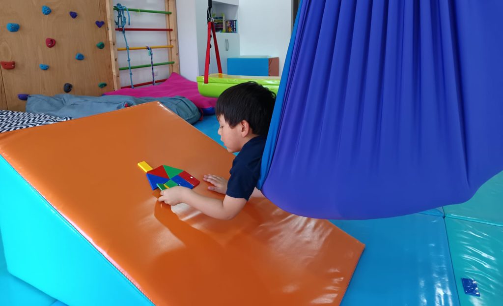 PractiKids, niño en un columpio terapéutico, participando en una sesión de terapia para trabajar el sistema vestibular y el equilibrio.